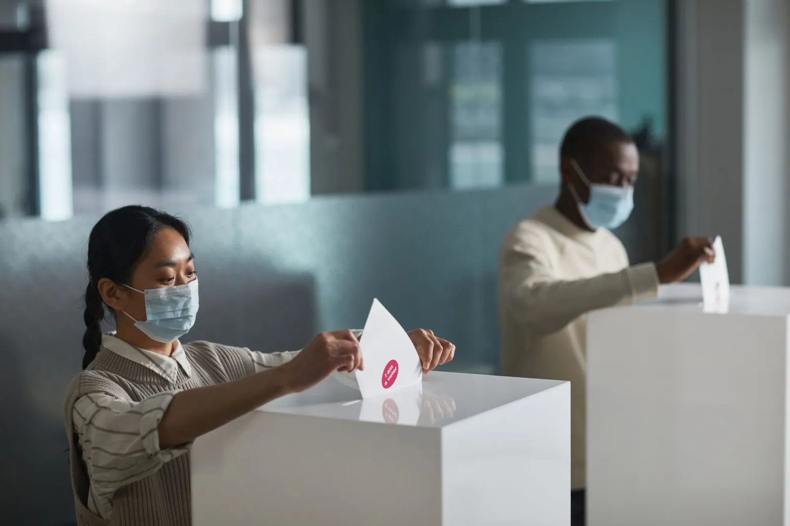 People casting ballots in an indoor election setting, practicing safety measures with masks.
